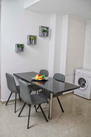 Une cuisine moderne avec un plan de travail noir, quatre chaises grises, un lave-linge et des plantes en pot accrochées au mur.
