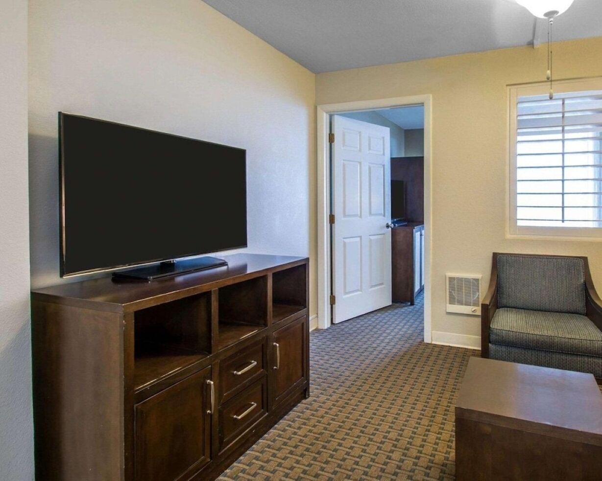 A room with a flat-screen TV on a wooden stand, a chair, and a door leading to another room.