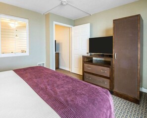 Ein Hotelzimmer mit Bett, Fernseher, Kleiderschrank und einer Tür zu einem weiteren Raum.