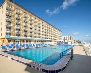 Ein Hotel mit großem Pool, mehreren Balkonen und blauen Liegestühlen.