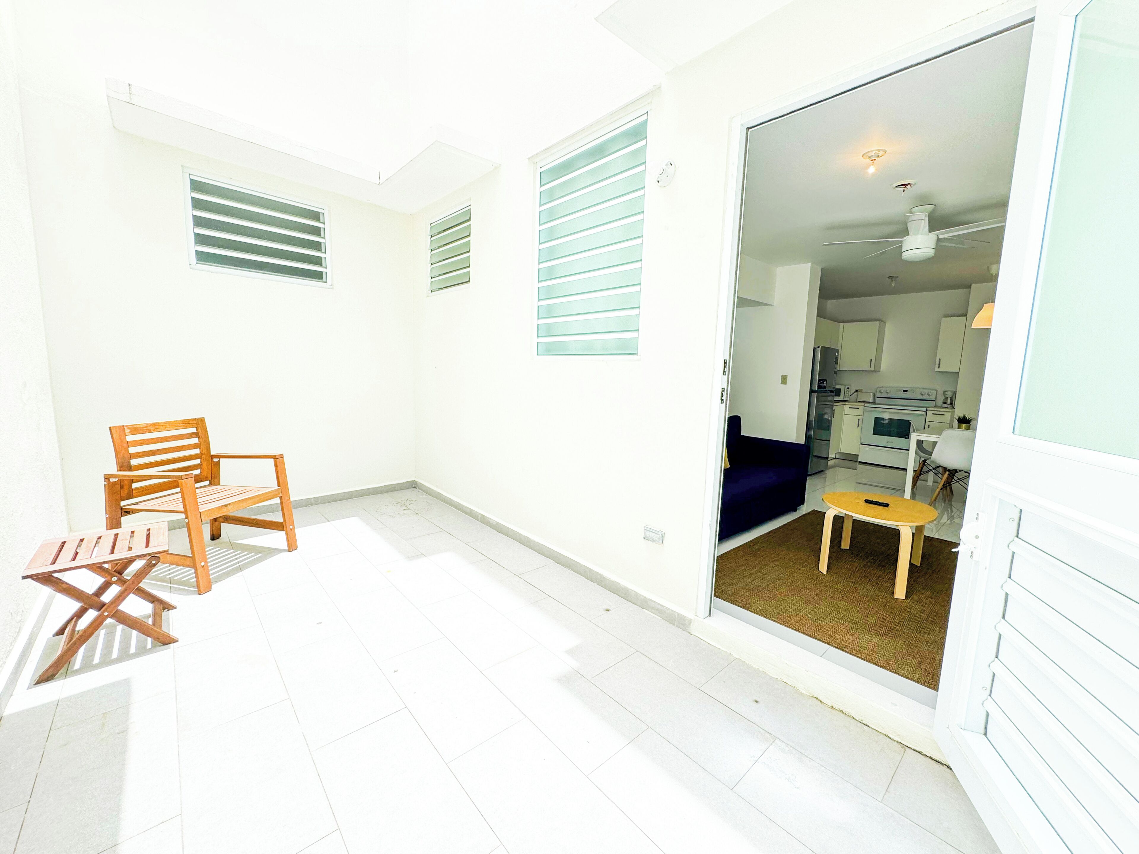 A room with a wooden chair, a small table, and a doorway leading to a kitchen area.