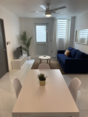 A modern living room with a white dining table, a blue sofa, and a ceiling fan. - Arecibo Hotel 2101 (Arecibo)