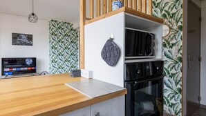 Ett modernt kök med en bänkskiva i trä, en mikrovågsugn och en ugn. På vänster sida finns en tv och på höger sida en tapet med mönster.