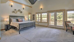 Ein Schlafzimmer mit einem großen Bett, einem Nachttisch, einem Sessel und Blick ins Freie durch eine Schiebetür.