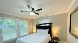 A bedroom with a bed, two bedside lamps, a ceiling fan, and two windows with blinds.