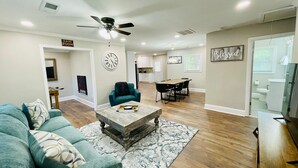 A spacious living room with a teal sofa, a wooden coffee table, and a dining area with a black table and chairs.