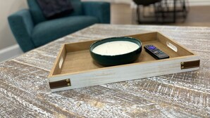 A wooden tray with a bowl of white substance and a remote control on a textured table.