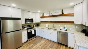 A modern kitchen with white cabinets, stainless steel appliances, and a wooden floor.