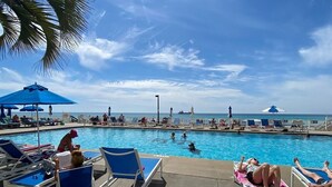Ein Poolbereich mit Liegestühlen und Sonnenschirmen, mit Blick auf einen klaren blauen Himmel und das Meer.
