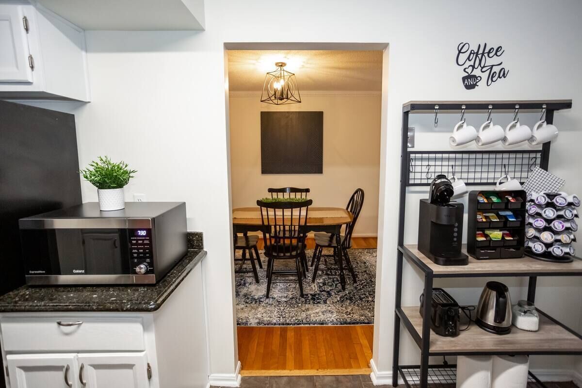 A compact kitchen with a microwave, a coffee station, and a dining area with a chandelier.