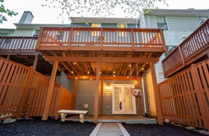 A covered patio area with a wooden deck, a bench, and a door leading to a building.