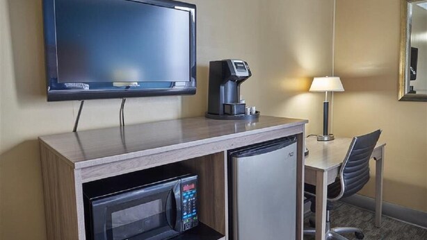 A hotel room with a flat-screen TV, a coffee maker, a microwave, a refrigerator, a desk with a chair, and a lamp. - Queen Bed Standard View (Fairhaven)