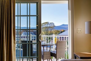 A room with a view of mountains, a balcony with wicker chairs, and a table.