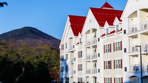 A multi-story hotel with a red roof, balconies, and a mountainous backdrop. - Lincoln NH | Ski Town Stay | Pool & Mountain Access (Lincoln)