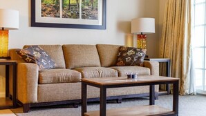 A living room with a sofa, a coffee table, two lamps, and a framed picture on the wall. - Lincoln NH | Ski Town Stay | Pool & Mountain Access (Lincoln)