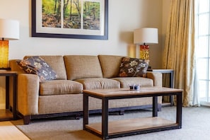 A living room with a sofa, a coffee table, two lamps, and a framed picture on the wall. - Lincoln NH | Ski Town Stay | Pool & Mountain Access (Lincoln)
