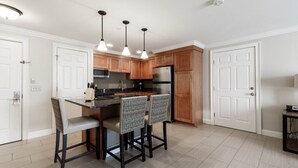 A modern kitchen with wooden cabinets, a stainless steel refrigerator, and a bar area with two chairs. - Lincoln NH | Ski Town Stay | Pool & Mountain Access (Lincoln)