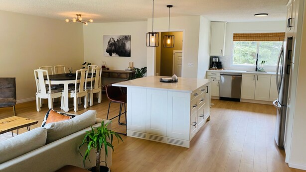 Une cuisine moderne avec des meubles blancs, un îlot central, des luminaires suspendus et un coin repas comprenant une table et des chaises.
