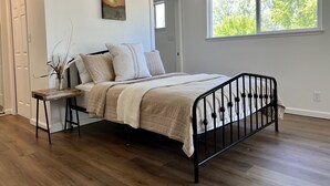 A bedroom with a bed, a window, a ceiling fan, and a painting on the wall.