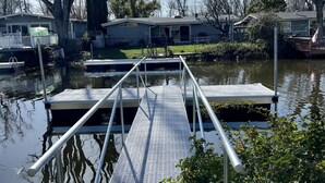 A dock leading to a house with a covered porch, surrounded by trees and a calm body of water.