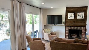 A living room with a fireplace, a television mounted above it, and a sliding glass door leading to an outdoor area.