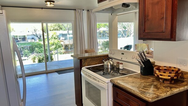 A kitchen with a stove, oven, and countertop. There is a window with curtains, and a view of the outside.