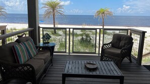 A covered deck with a wooden table and two chairs, overlooking a beach with palm trees and the ocean. - Beachfront--Beachfront- Driftwood Yard (Mexico Beach)