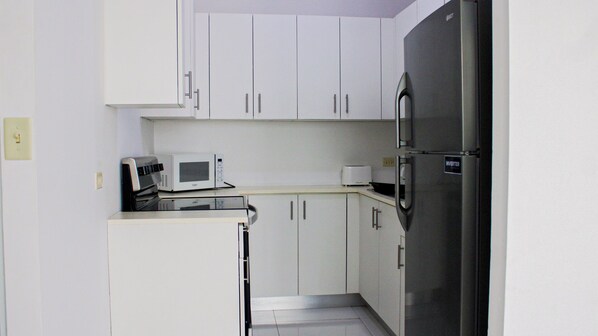 A compact kitchen with white cabinets, a stainless steel refrigerator, a microwave, and a toaster. - Arecibo Hotel 2104 (Arecibo)