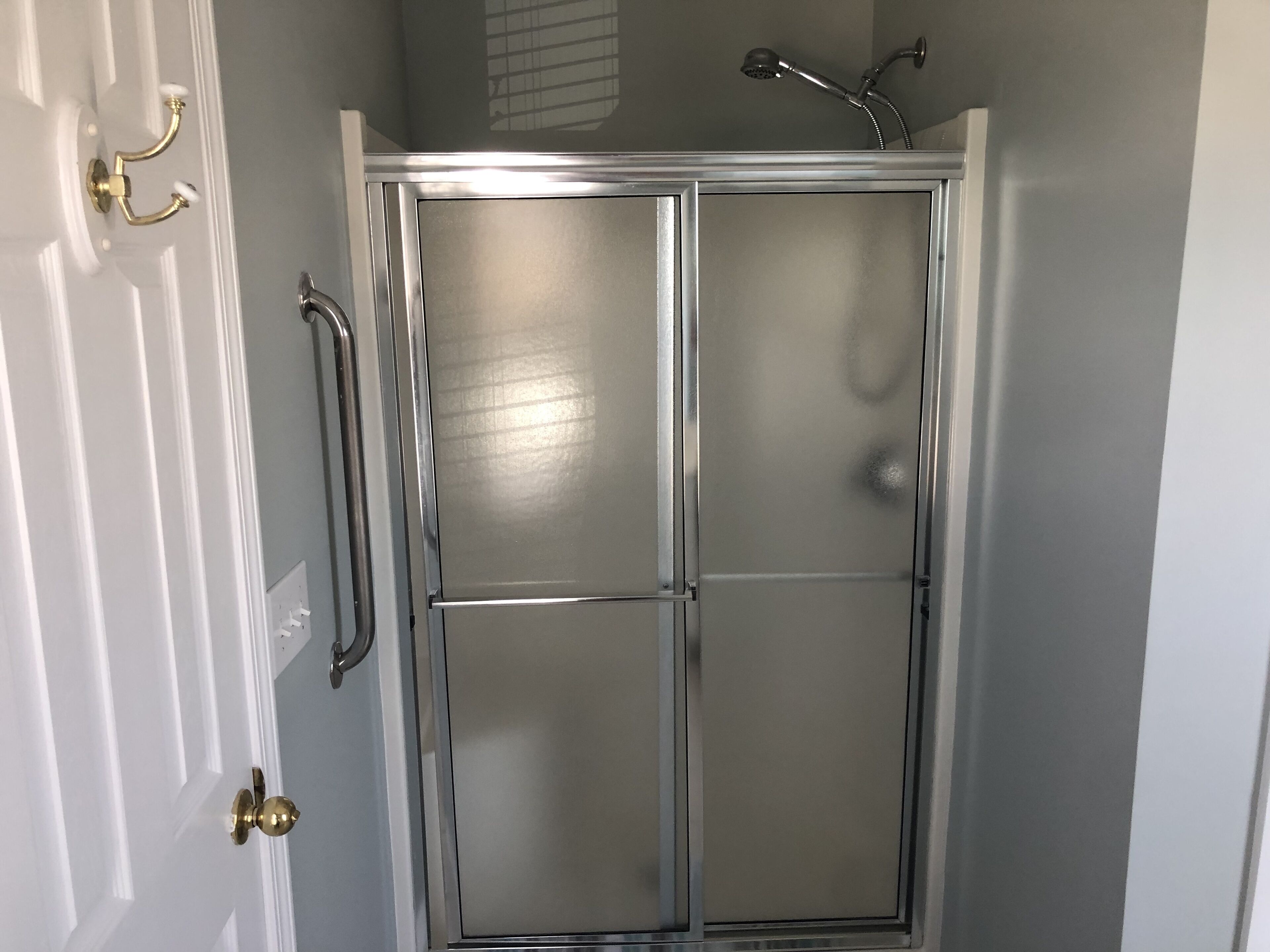 A shower enclosure with a frosted glass door, a showerhead, and a towel rack.