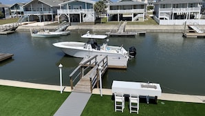 A marina with boats docked, a small dock with a lifebuoy, and houses in the background. - Canal House, New Bar/TV Area w/ view of water, Fenced yard & 5 Min Walk To Beach (Ocean Isle Beach)