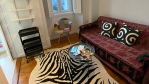 Ett vardagsrum med en zebramönstrad matta, en soffa med mönstrade kuddar, ett litet bord med böcker, en stol och en vit hylla.
