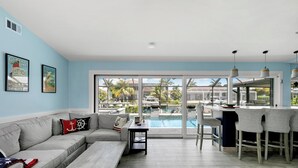 A modern living room with a large window, a pool, and a bar area. - Island Retreat .6 miles from the beach! (Marco Island)