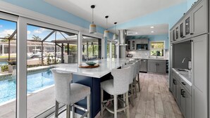 A modern kitchen with a large island, bar stools, and a view of a swimming pool. - Island Retreat .6 miles from the beach! (Marco Island)
