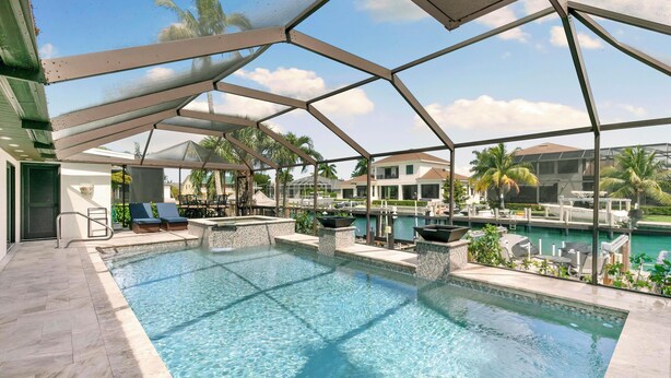 An outdoor swimming pool with a glass enclosure, surrounded by lounge chairs and a view of a marina. - Island Retreat .6 miles from the beach! (Marco Island)