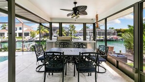 A sunlit patio with a dining table and chairs, overlooking a pool and a marina. - Island Retreat .6 miles from the beach! (Marco Island)
