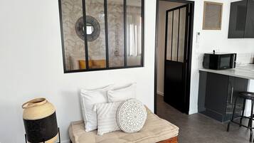 Een moderne woonkamer met een bank, een decoratieve spiegel en een keukenhoek met een magnetron.