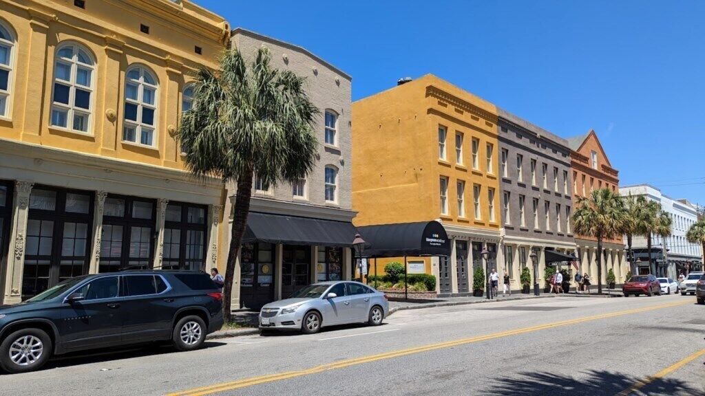 A street with historic buildings, parked cars, and pedestrians.