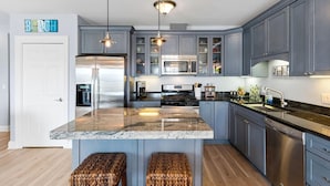 A modern kitchen with a central island, stainless steel appliances, and blue cabinetry.
