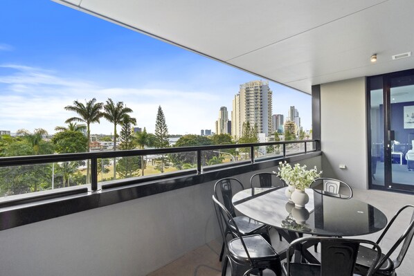 A balcony with a round table and chairs, a vase with flowers, and a city view.