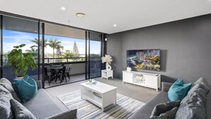 Un salon moderne avec un canapé gris, une table basse blanche et une grande fenêtre donnant sur la ville.