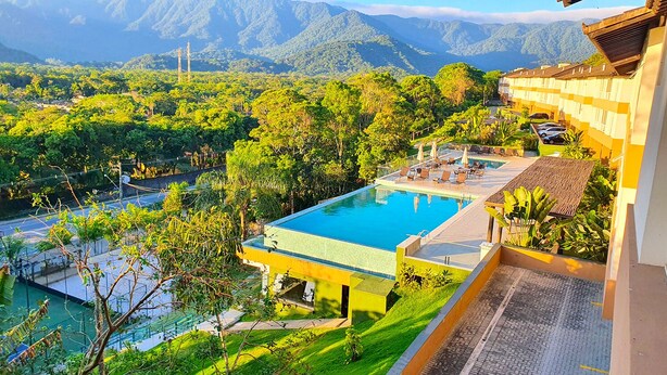 Ein Hotel mit Schwimmbad, umgeben von üppiger Vegetation und Bergen im Hintergrund.