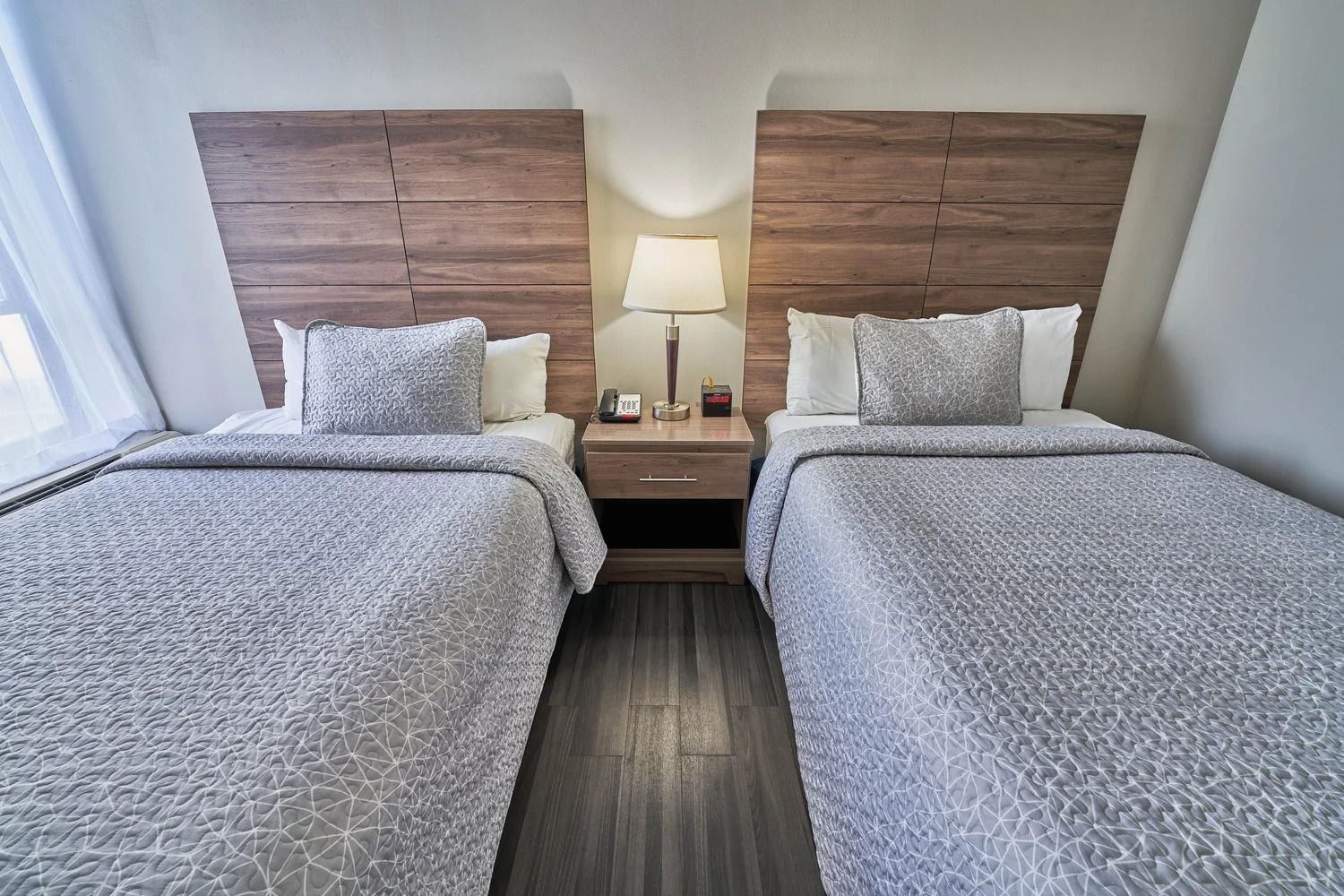 A hotel room with two beds, a nightstand with a lamp, and a wooden headboard.