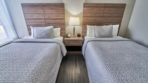 A hotel room with two beds, a nightstand, a lamp, and a window. - Two Double Beds - Standard (Fairhaven)
