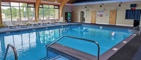 Una piscina interior con techo de madera, ventanas de vidrio transparente y un letrero de advertencia para salvavidas.