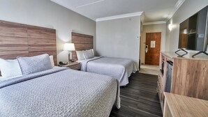 A hotel room with two beds, a desk with a lamp, a TV, and a wooden cabinet. - Two Double Beds - Standard (Fairhaven)
