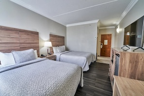 A hotel room with two beds, a desk with a lamp, a TV, and a wooden cabinet. - Two Double Beds - Standard (Fairhaven)