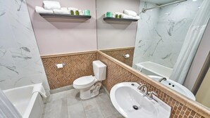 Un baño con inodoro, lavamanos y bañera. Hay barras para toallas sobre el inodoro y el lavamanos.