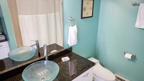 Un baño con lavamanos de vidrio, inodoro blanco y perchero para toallas.