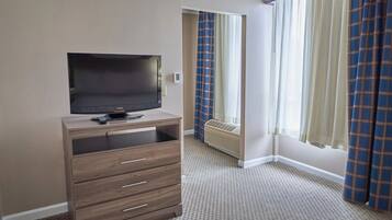 A hotel room with a flat-screen TV on a wooden cabinet, a window with curtains, and a radiator.