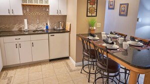 Una cocina con armarios blancos, salpicadero de azulejos y un comedor con mesa para cuatro.